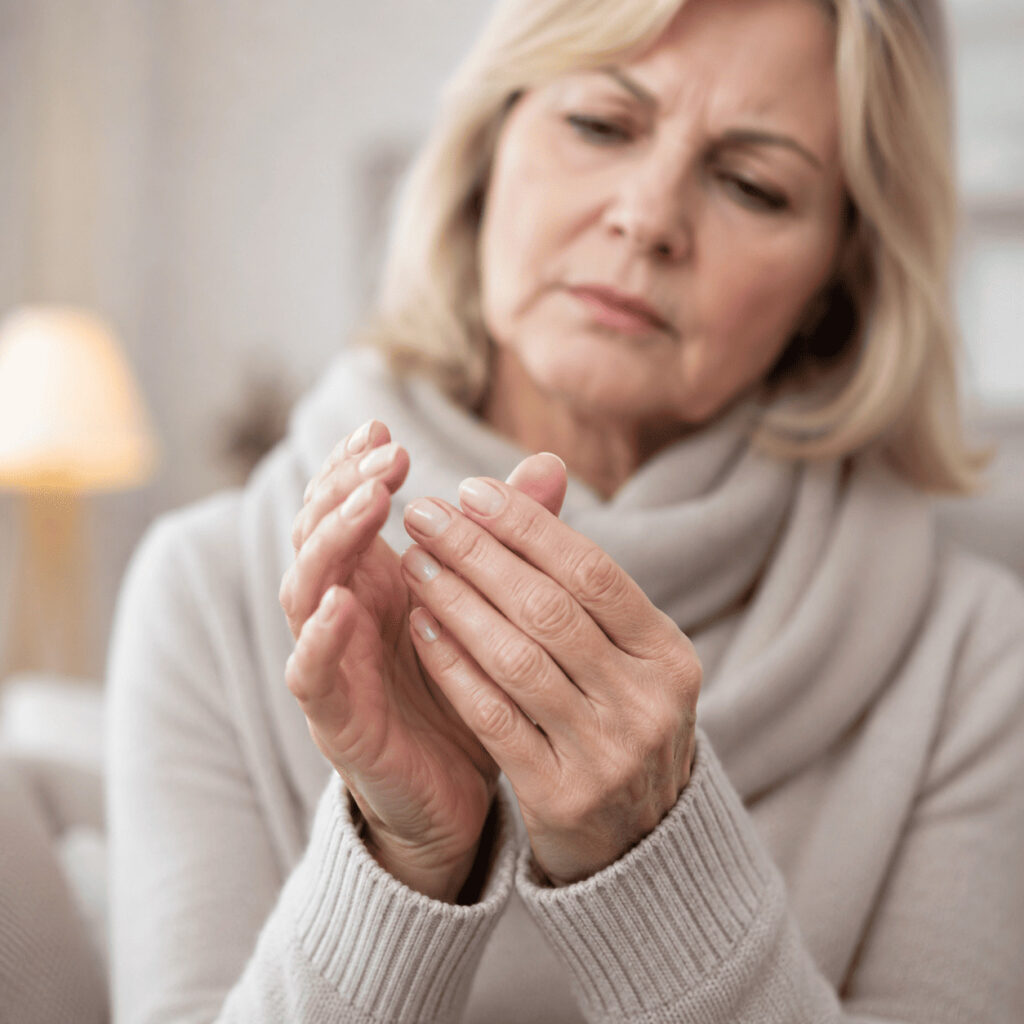 Femme senior se touchant les mains froides, signe possible d’une mauvaise circulation sanguine aux extrémités.