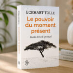 Livre Le Pouvoir du moment présent d’Eckhart Tolle, présenté debout sur une table dans une ambiance calme et lumineuse.